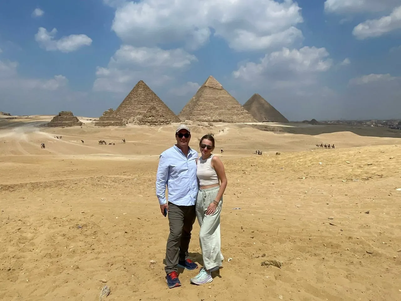 Two travellers standing in the desert in front of the Pyramids of Giza